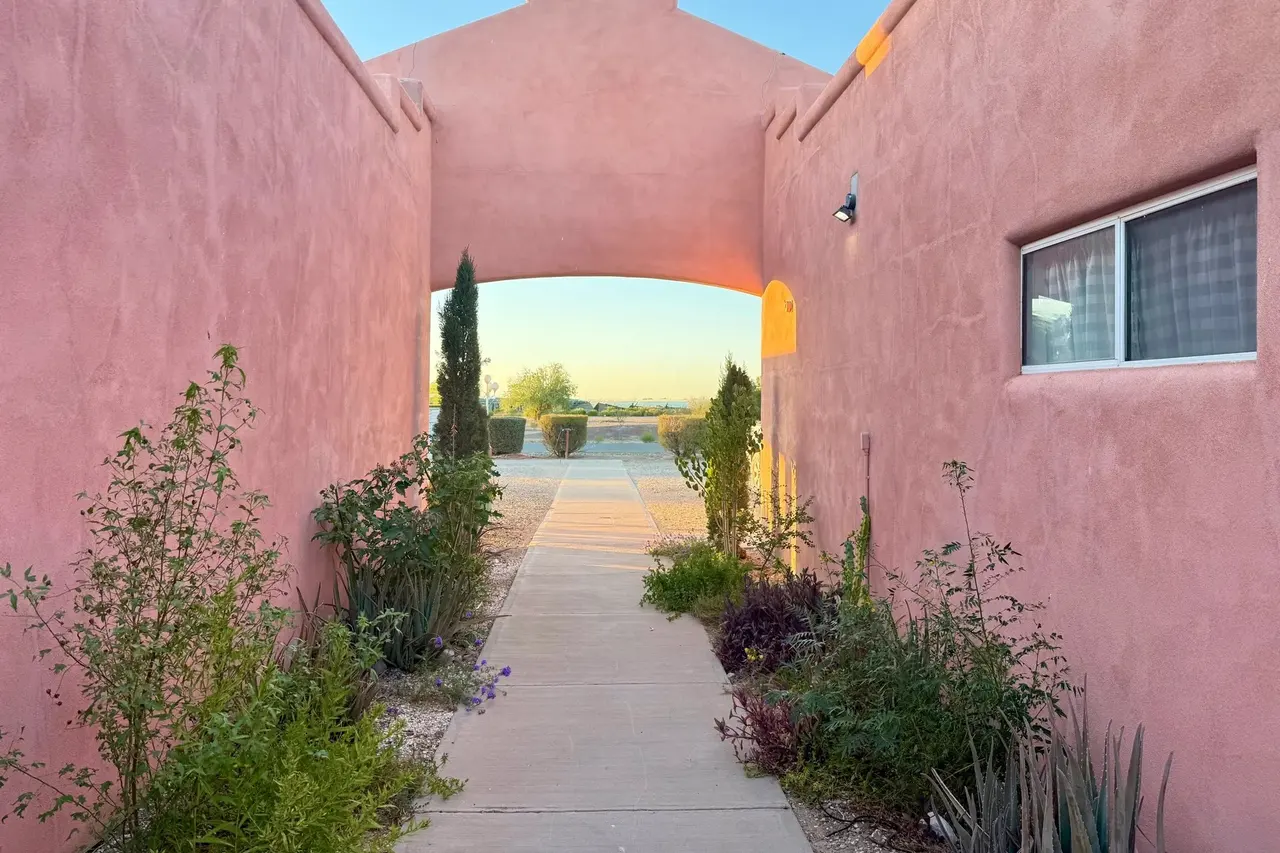 A walled adobe passage glowing rose at dusk, opening onto the desert
