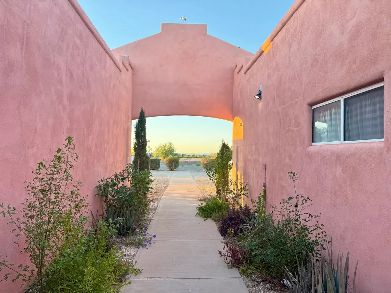 A walled adobe passage glowing rose at dusk, opening onto the desert