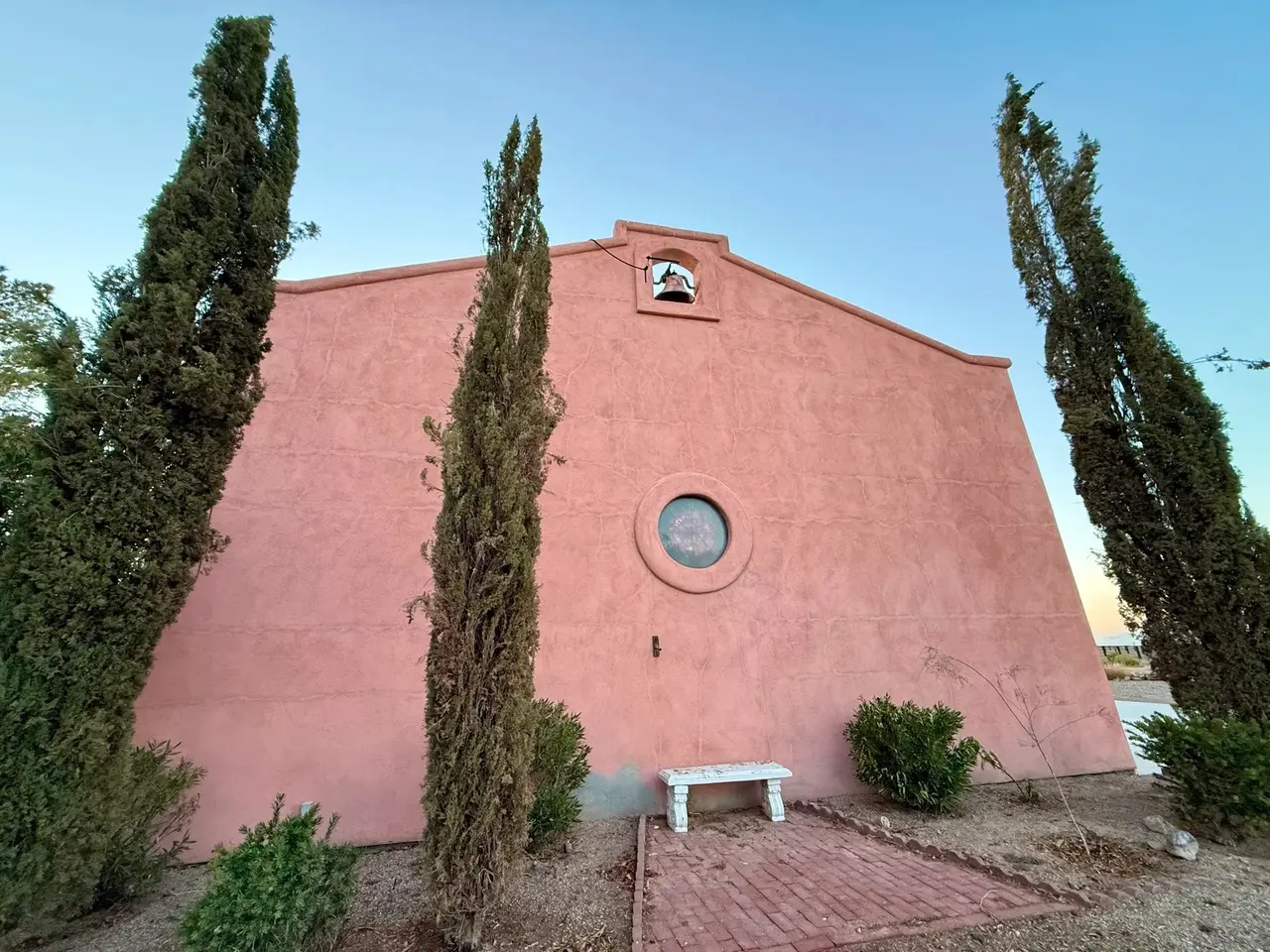 Rose-colored gable wall with a round window, flanked by two cypress trees