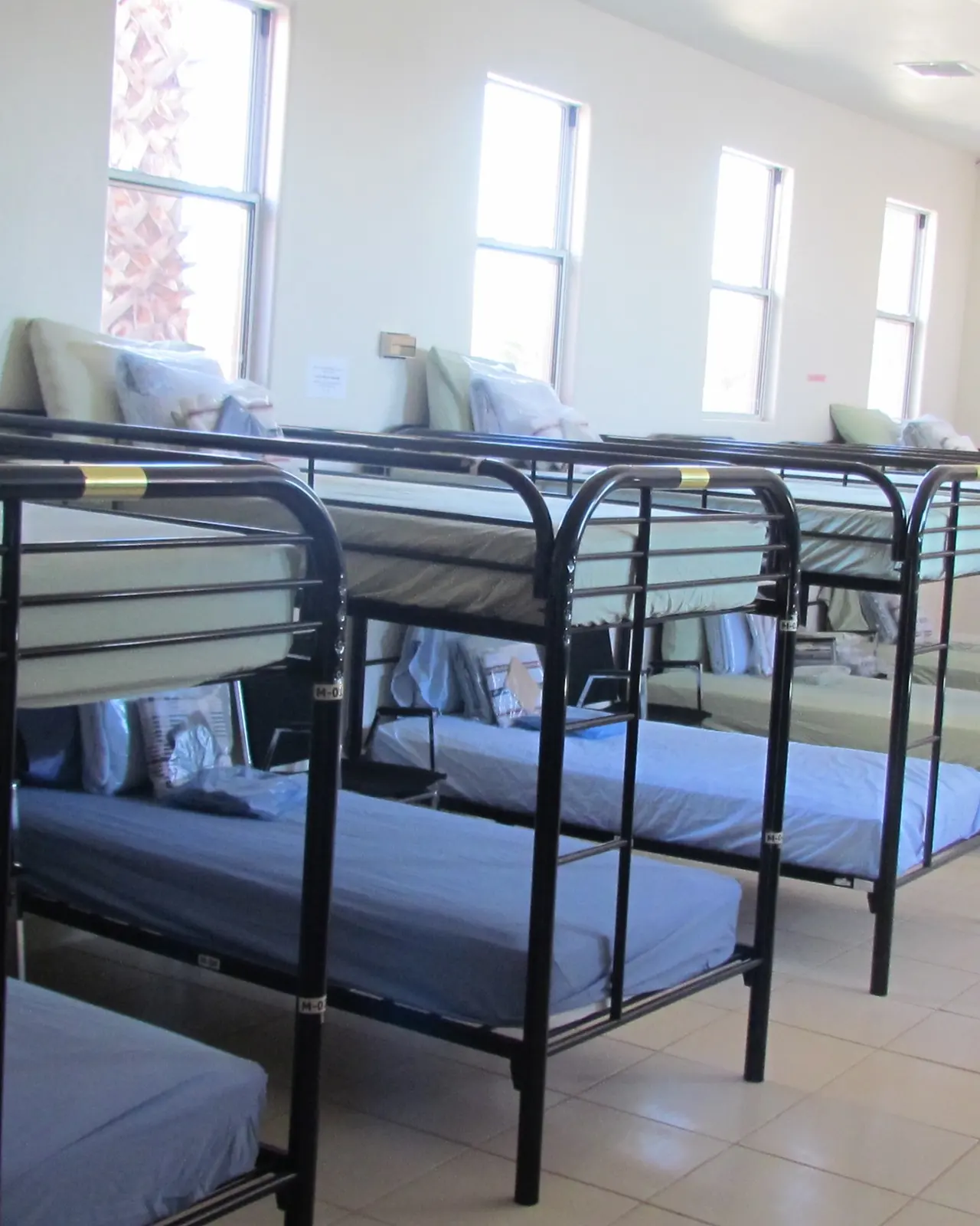 A bright dormitory room lined with made-up bunk beds
