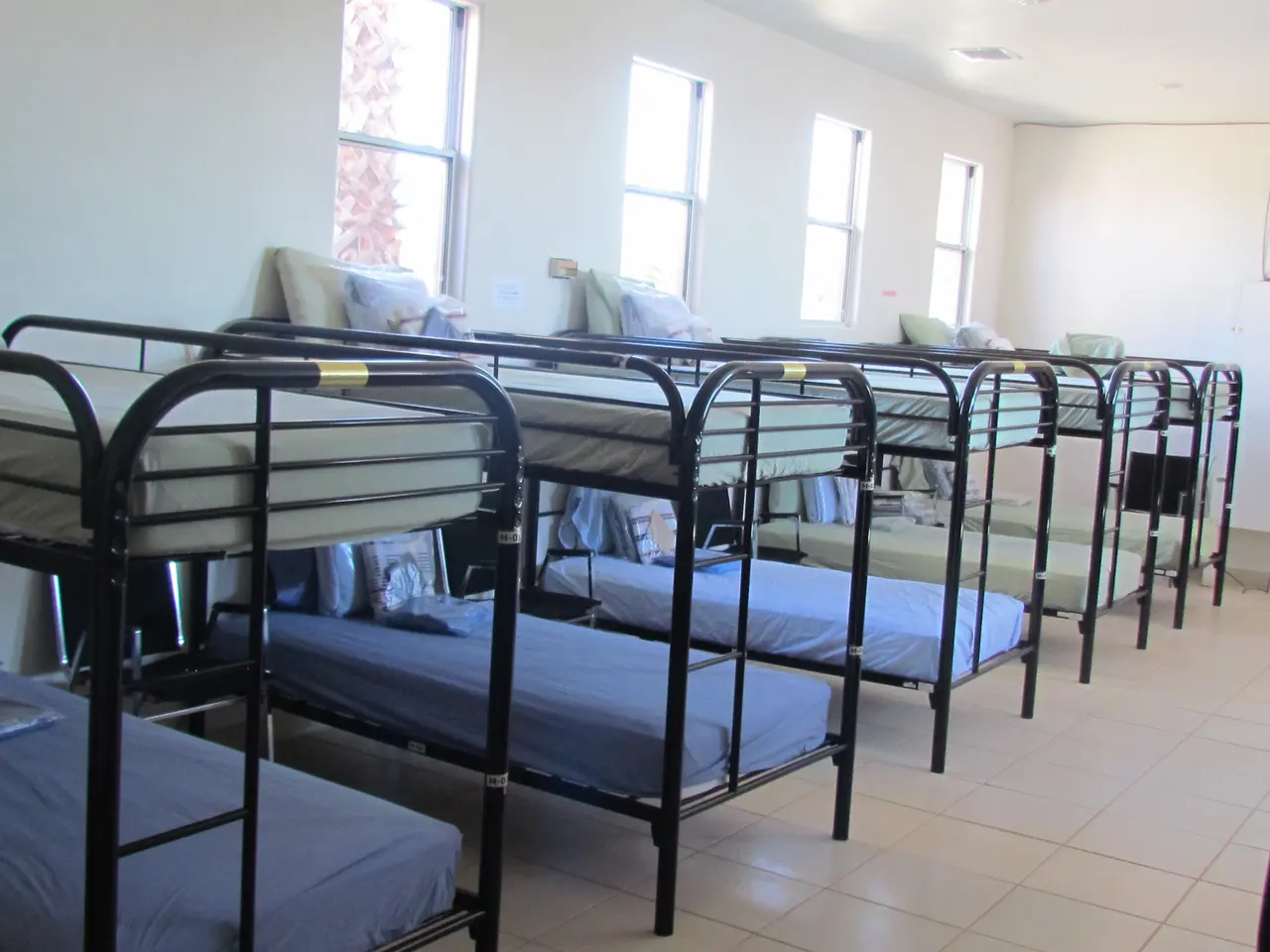 A bright dormitory room lined with made-up bunk beds