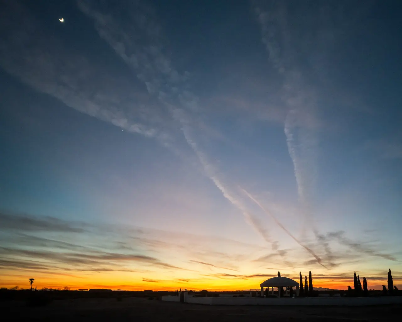 Contrails crossing an indigo dusk sky above the horizon