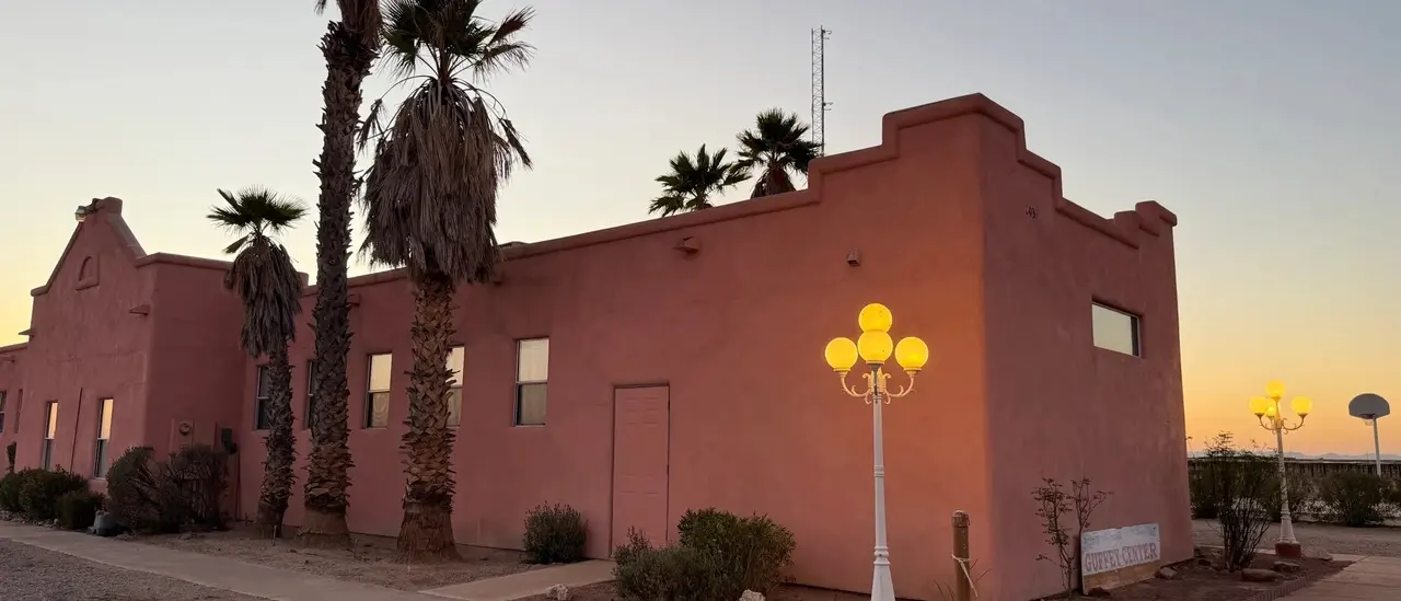 The meeting hall's stepped adobe facade and palms at sunset, a globe lamp lit