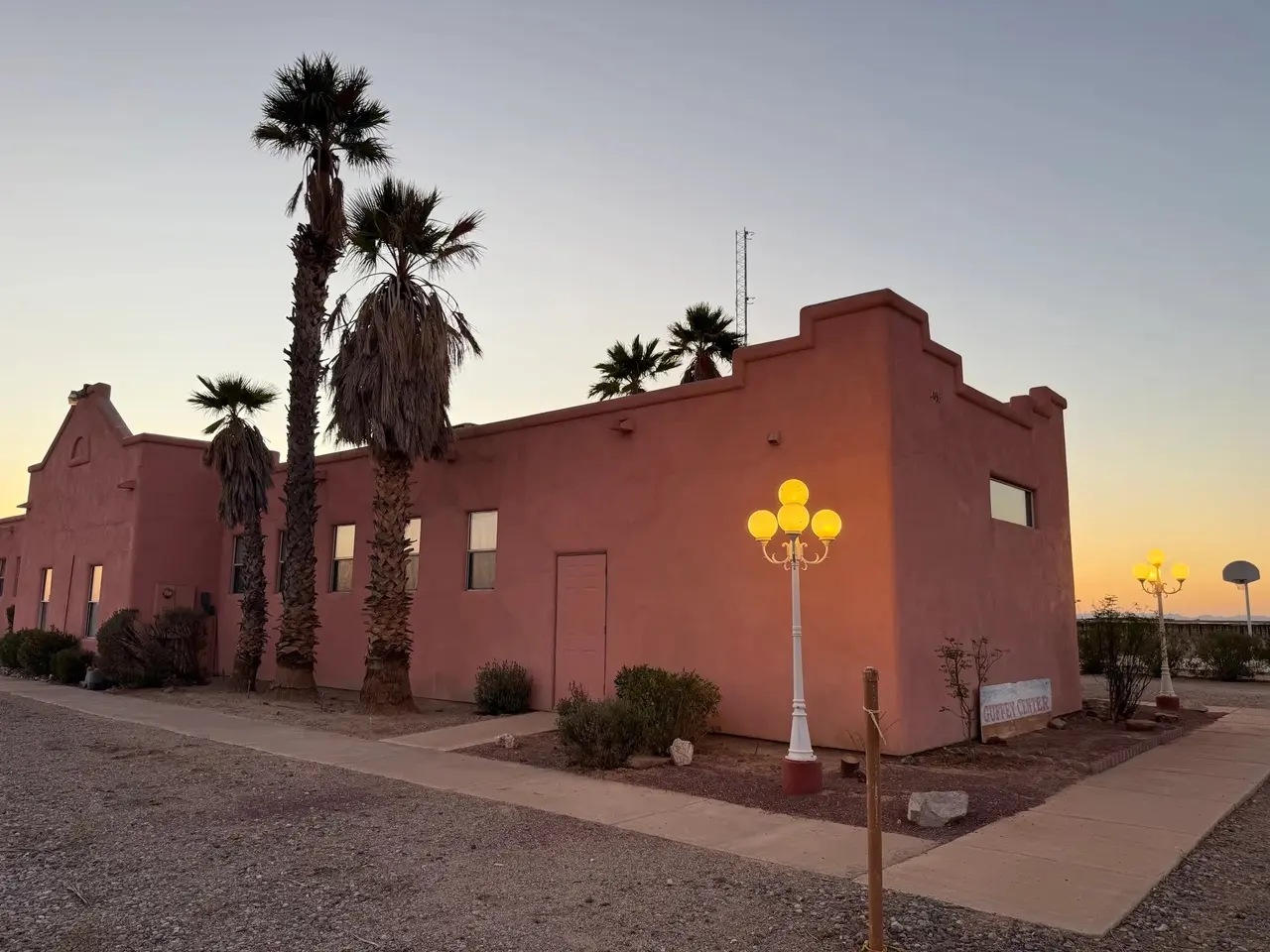 The meeting hall's stepped adobe facade and palms at sunset, a globe lamp lit