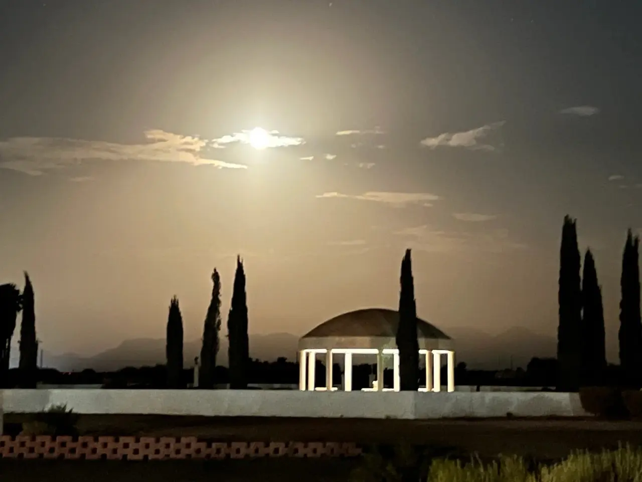 A domed pavilion glowing under a bright moon, cypress silhouettes around it