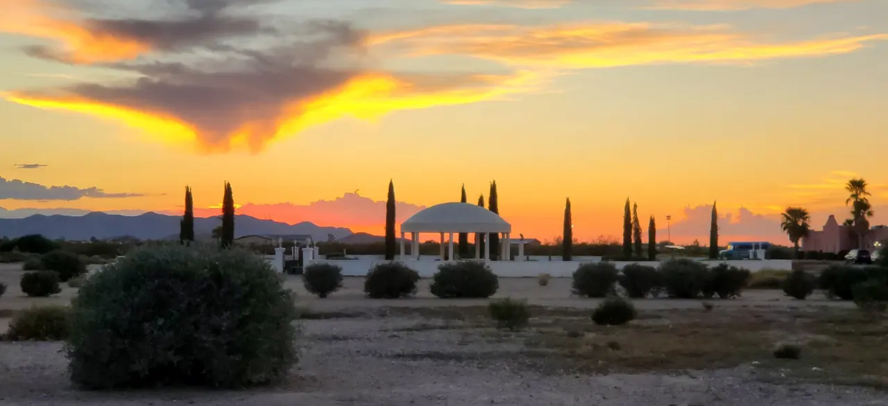 Fiery sunset clouds over the desert, cypress trees and a domed pavilion